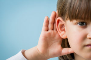 a young girl with her hand up to her right ear, intently listening to something directly ahead.