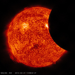 The Moon appears as a black disk and the Sun is a fiery ball of swirling red and orange. In this image, the Moon is slowly moving out of the Sun’s way. It blocks only a small area on the right side of the Sun.
