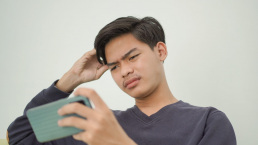 Asian man looking confused while staring at his phone.
