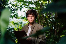 Young person standing still among the trees observing while holding a clip board.