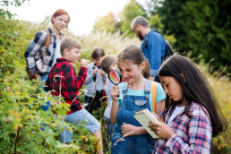 A group of children with adults observing and taking notes in nature.