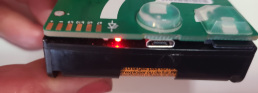 The edge of a AudioMoth device with a single red light flashing to the left of the Micro USB port location