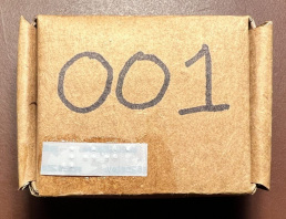 Small square cardboard box with the number 001 written in large print and a braille label attched in the bottom left corner.