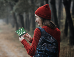 Woman holding an AudioMoth on a hiking path in a wooded area