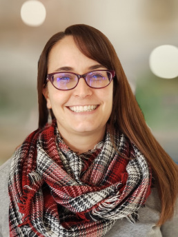 Woman with a broad smile wearing glasses and a thick scarf.