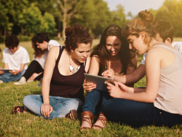 group of three female presenting friends sitting and taking notes together outside on the grass
