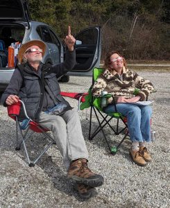 Two people sitting in folding chairs with eclipse glasses on.