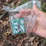 hand holding a small electronic device encased in a plastic bag.